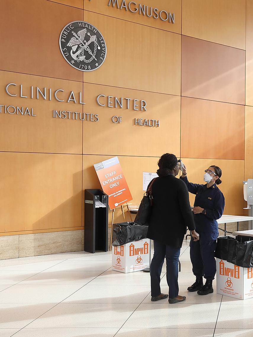 Uniformed worker takes temperature of an employee entering building.
