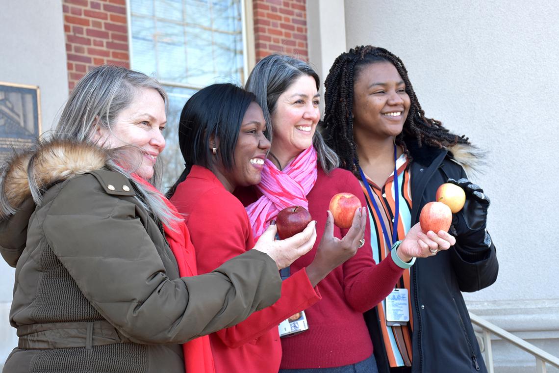 Four women smile as they hold up apples.