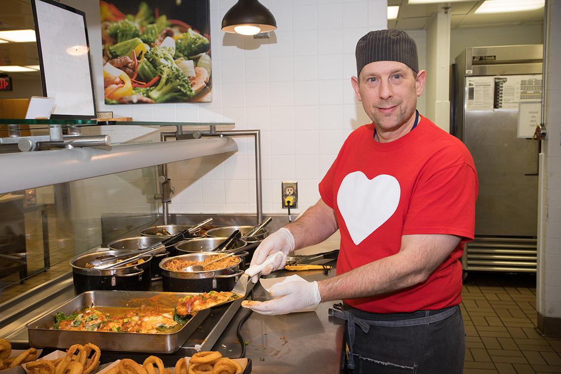 Man in chef's clothing holds a spatula with fish on it.