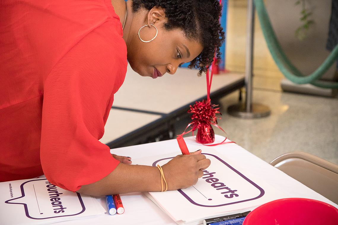 Woman leans over table to sign a poster-size pledge card.