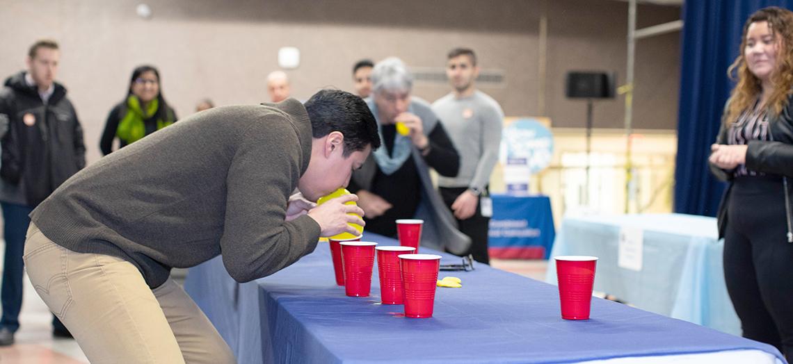 Flores blows air into a yellow balloon over red plastic cups on a table.