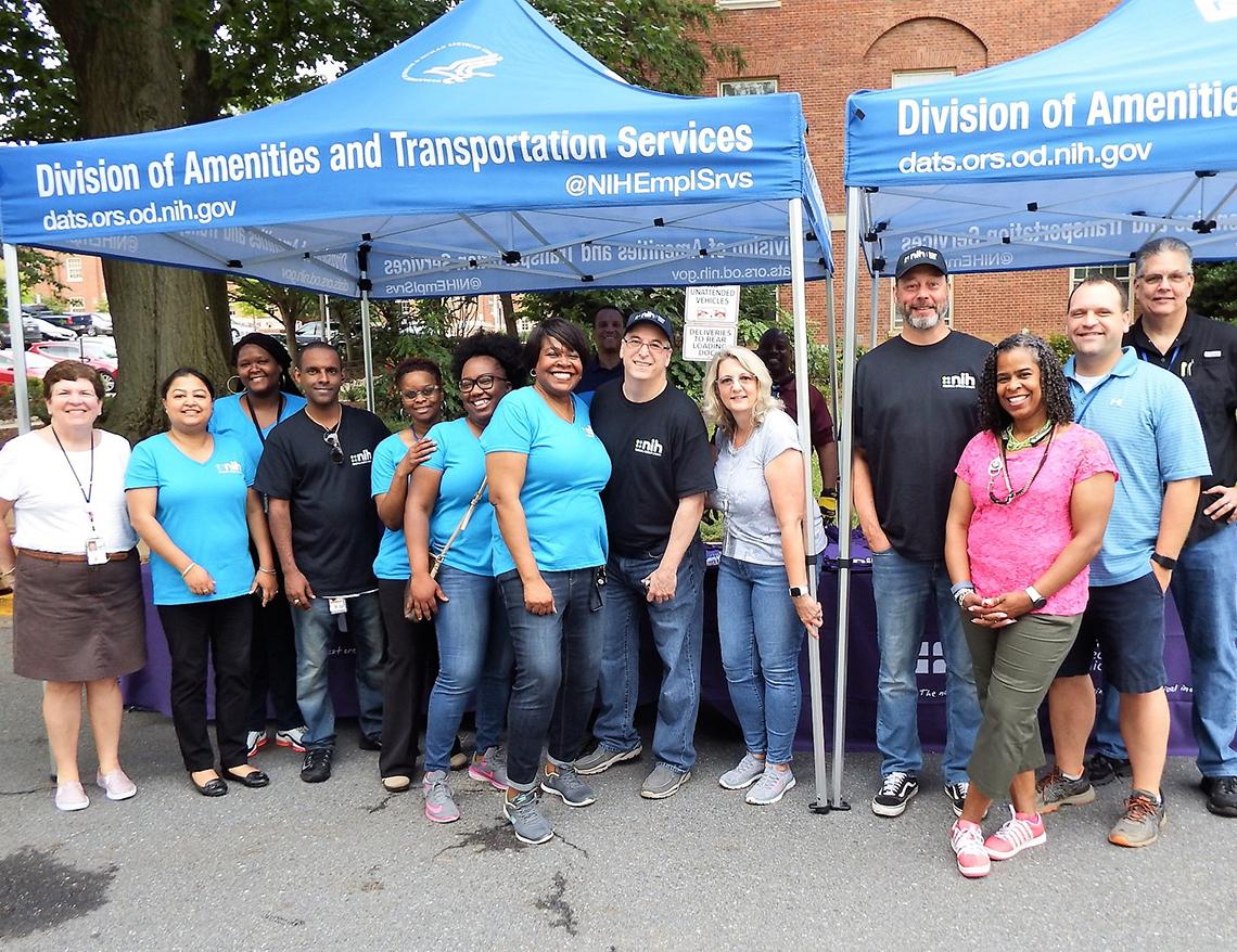 Staff from NIHFCU stand under two blue canopies
