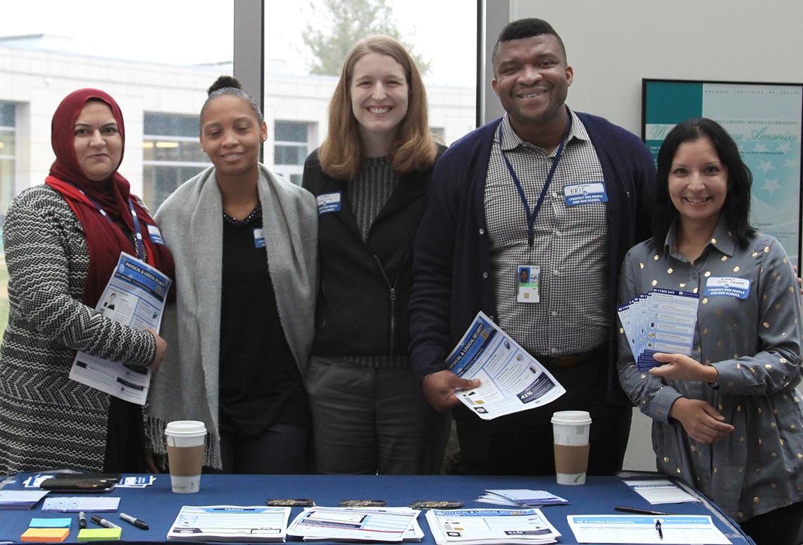 A smiling group of NIH'ers stand at an information table.