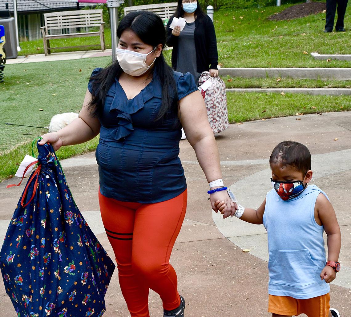 A woman holds a little boy's hand.