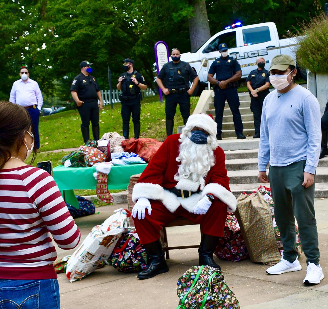 A woman takes a photo with her iphone of a young man wearing a blue longsleeve shirt and Santa.