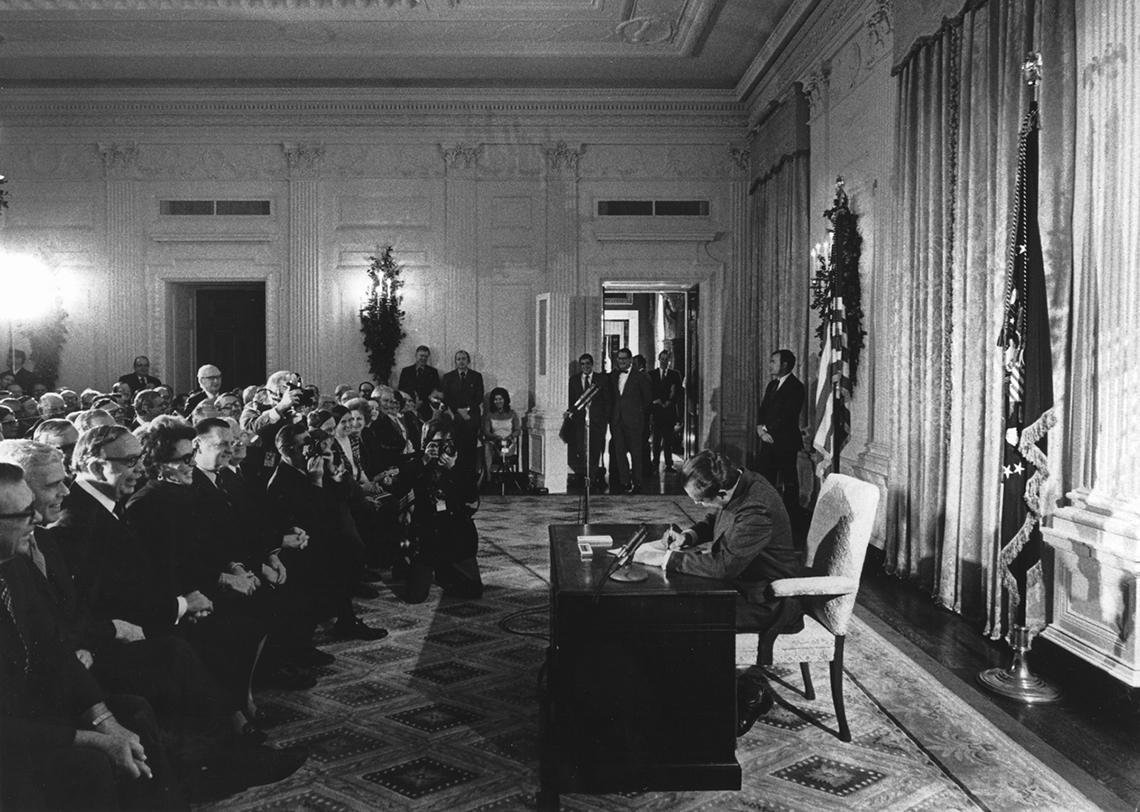 Nixon signs the act in a front of a crowd in a White House room