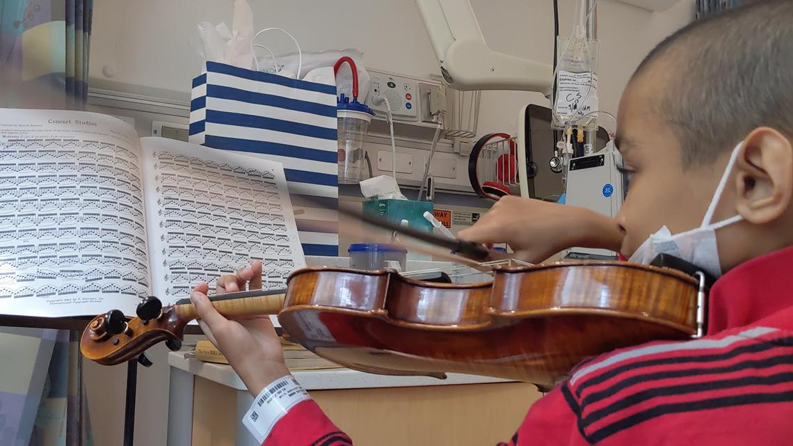 Photo from behind shows Caesar with bow to violin, reading sheet music, in his hospital room