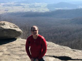 Steve Friedman, in red sweatshirt and sunglasses, stands atop Old Rag Mountain