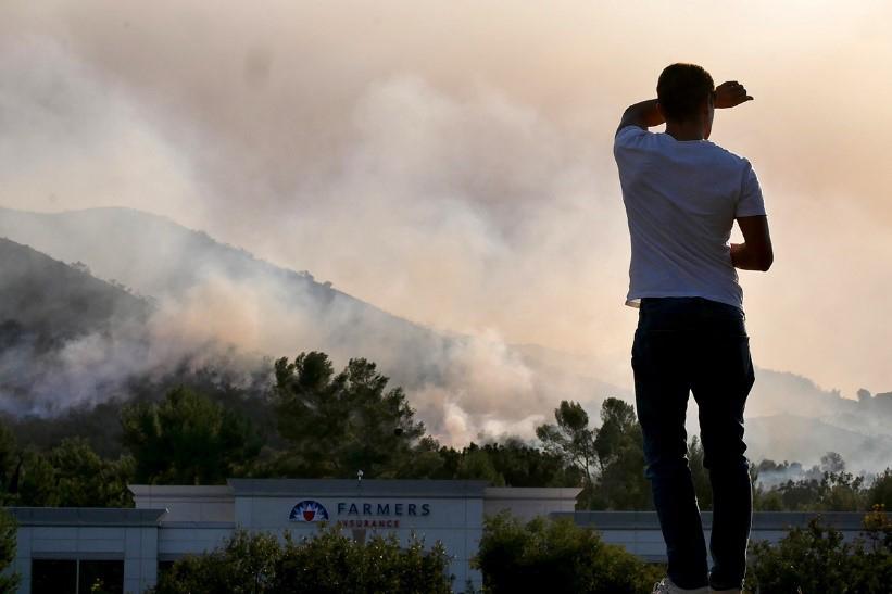 A man looks towards a mountain covered in heavy wildfire smoke