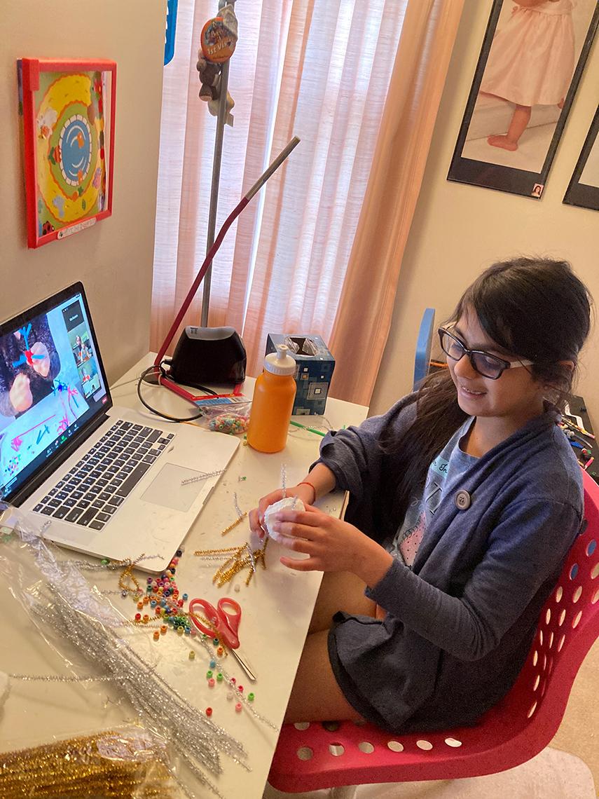 Dia sits at a computer desk while making arts and crafts