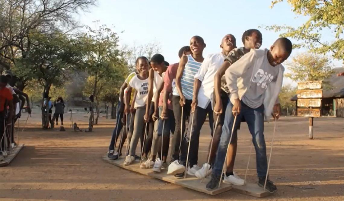 Children laugh while helping each other balance on a long board during a team exercise in Botswana in Africa.