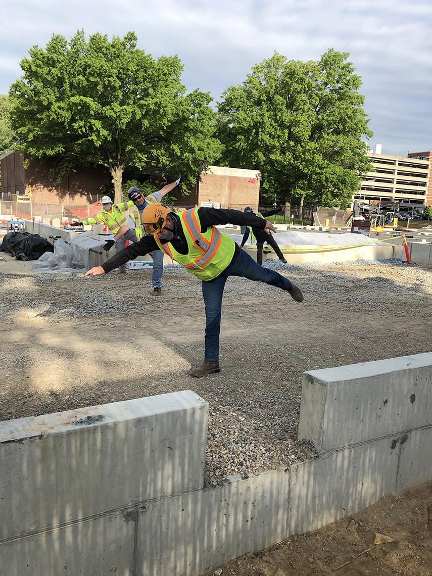 Close up view of individual construction worker standing on one leg with the other leg and one arm stretched out.