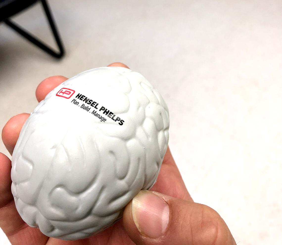Close up of hand holding an oblong-shaped stress ball with company name printed on it.