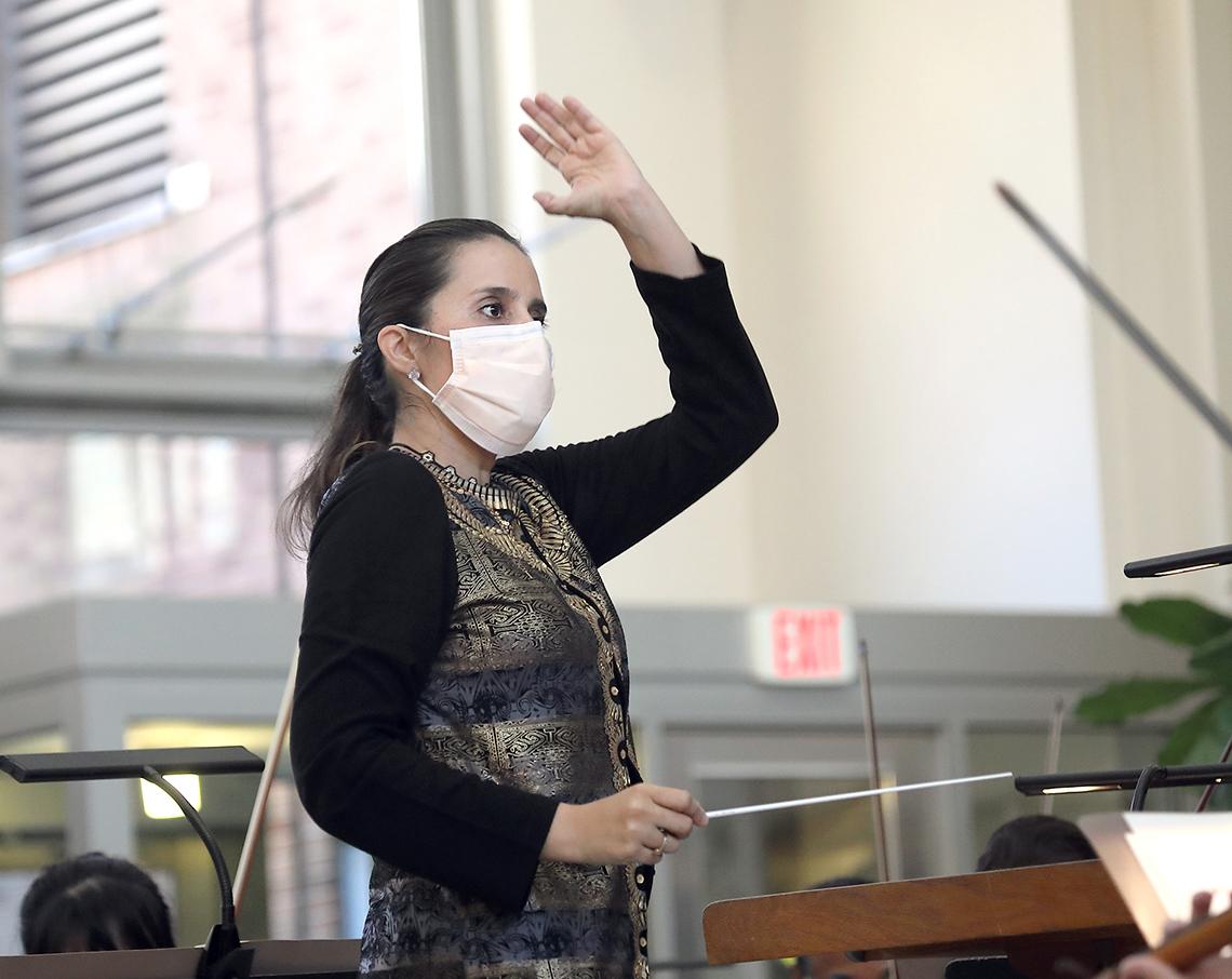 Gonzalez-Granados stands at podium, fingers curled around baton, with other hand raised above her head