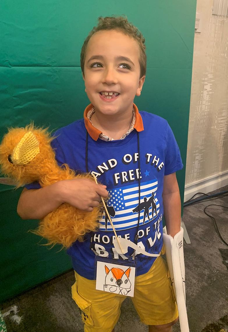 A young smiling boy holds his yellow plushie.