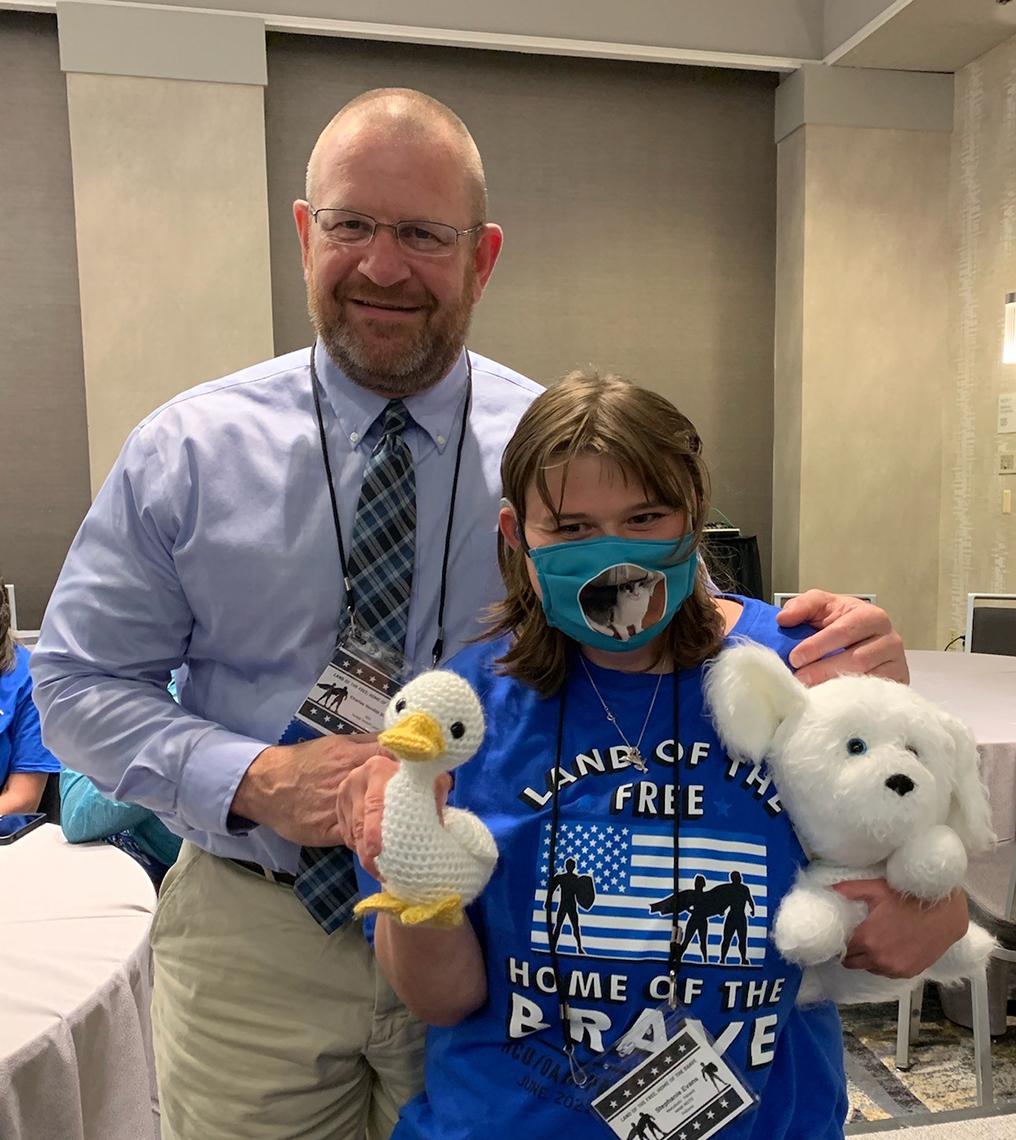 Dr. Venditti stands smiling with Stephanie, a patient holding up her dog and duck plushies.