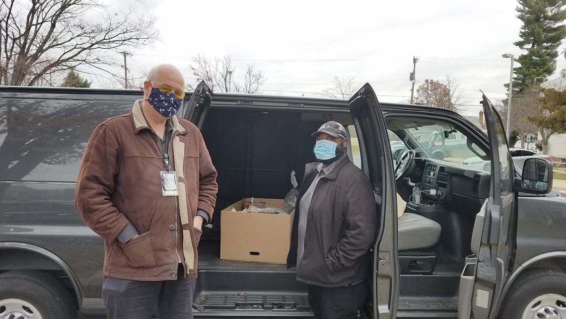 Masked up Hawk and Shubert in front of open cargo van doors