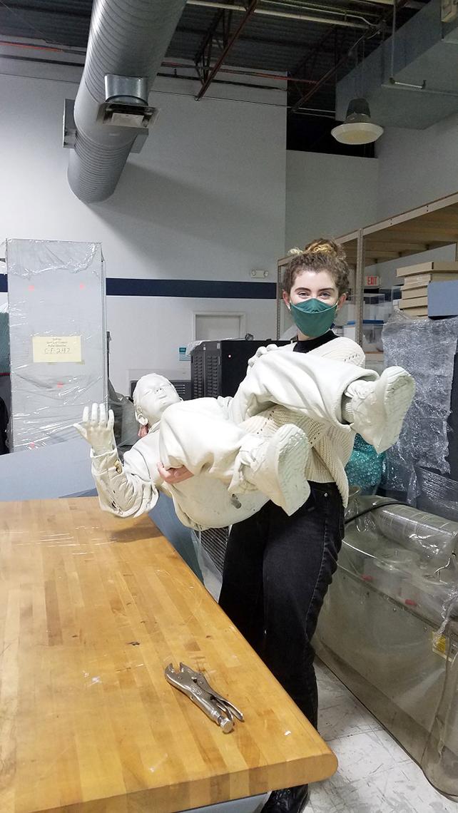 Masked young woman holds a sculptured figure.