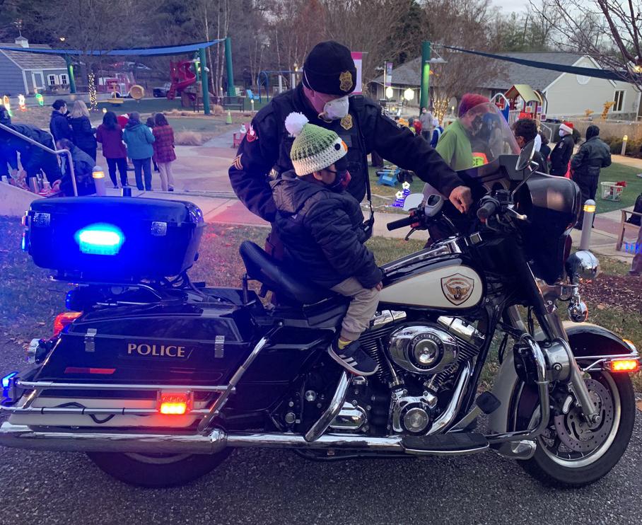 A young boy sits atop a police motorcycle as the officer stands by him, explaining its features.
