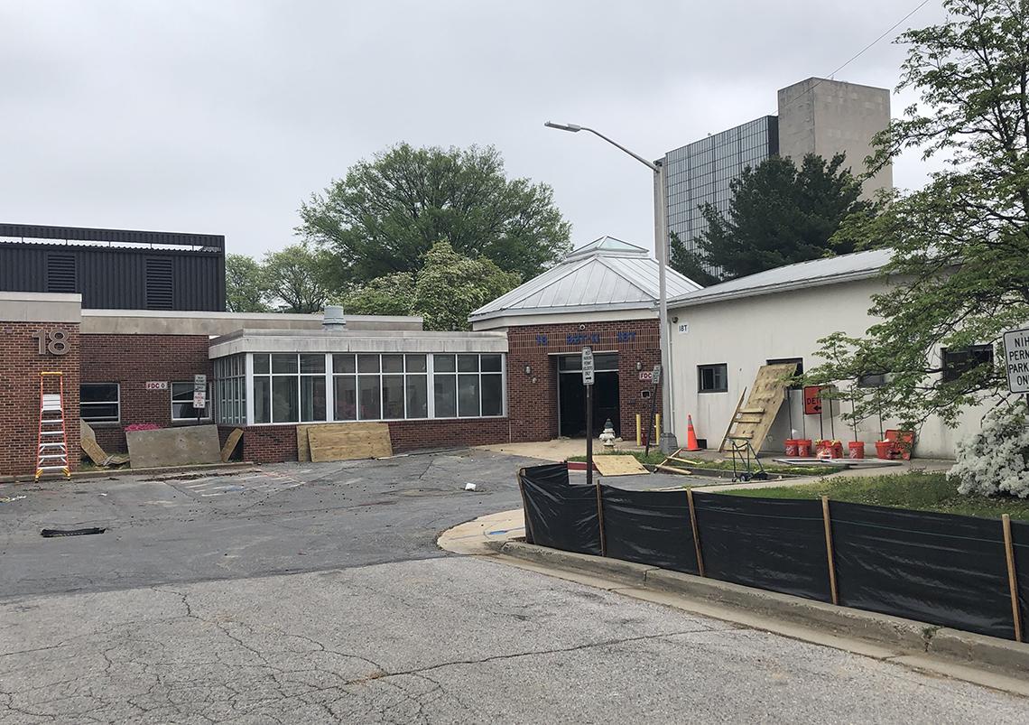 A photo of bldg. 18, a small, one-story brick lab building, with wood planks, a ladder and temporary fencing