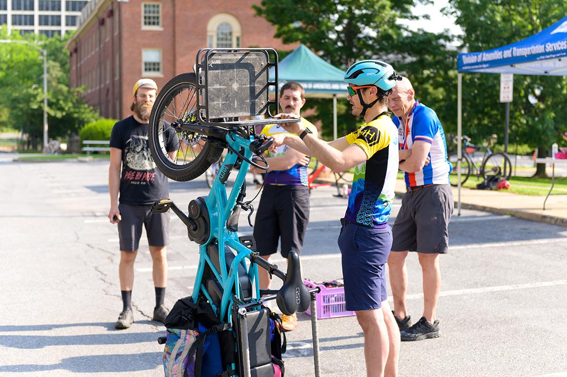 Biker in helmet stands bike on rear wheel, with front basket and saddle bags showing