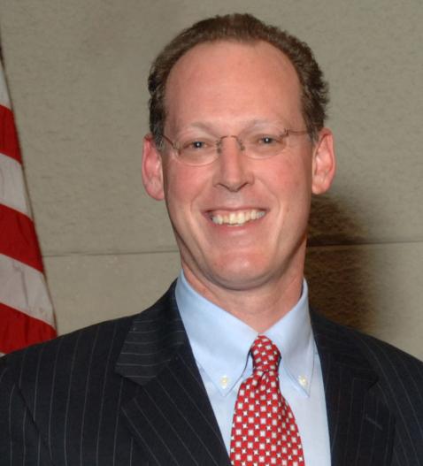 Head shot of Farmer, smiling, standing beside U.S. flag