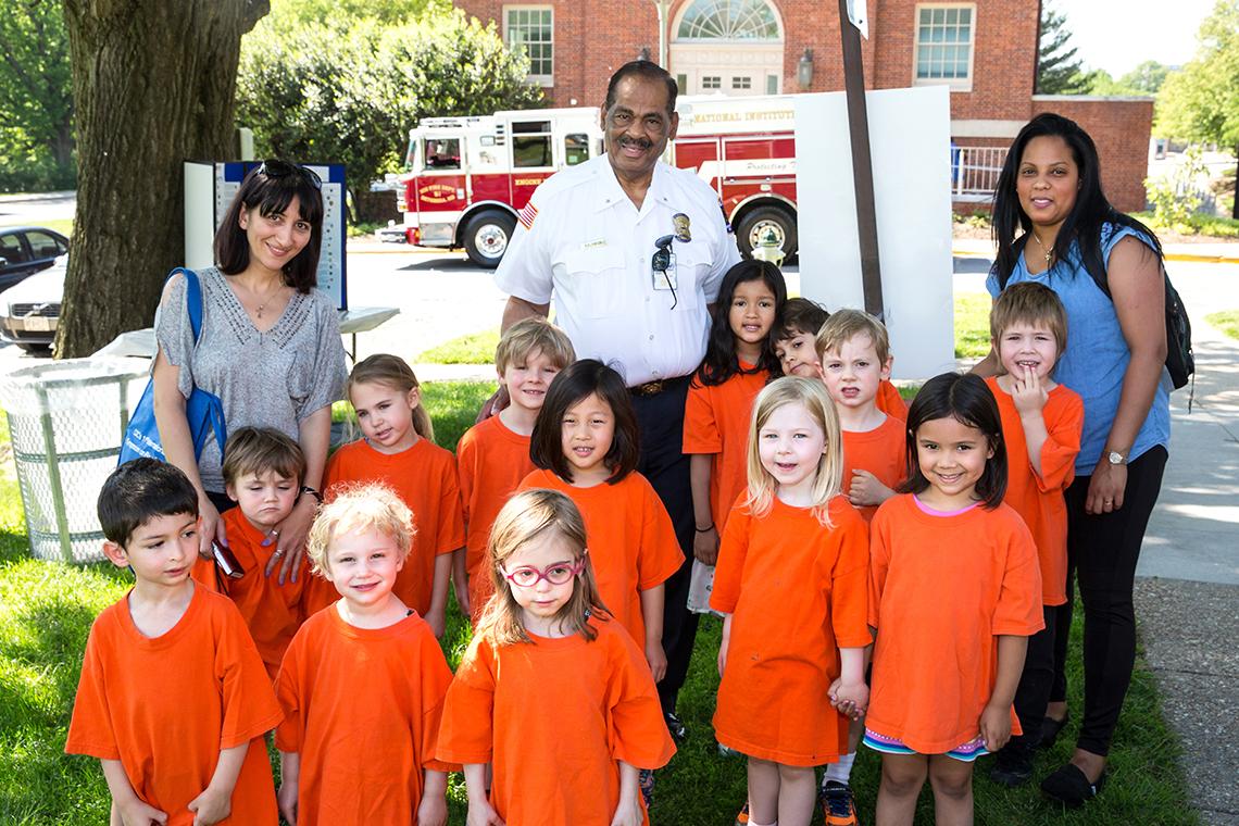 Hinon poses for a photograph with preschoolers wearing orange shirts with their two chaperones in front of a fire truck