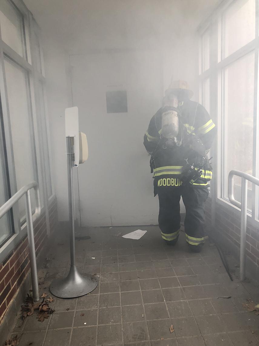 Firefighter in gear with helmet, with back toward camera, in smoke-filled entry