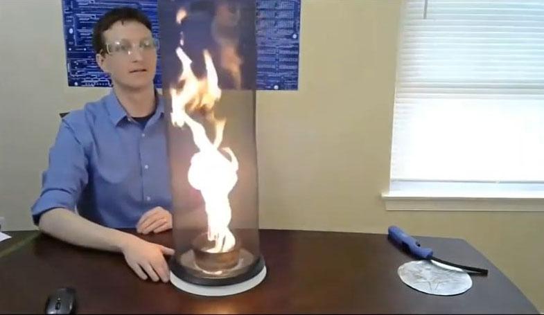 Rohde seated at table attends to an open flame contained in a glass cylinder.