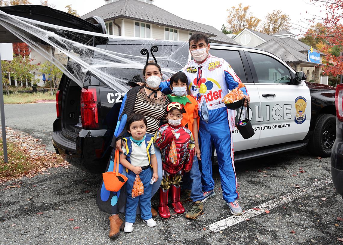 Costumed family poses in front of a police vehicle adorned with fake spider web.