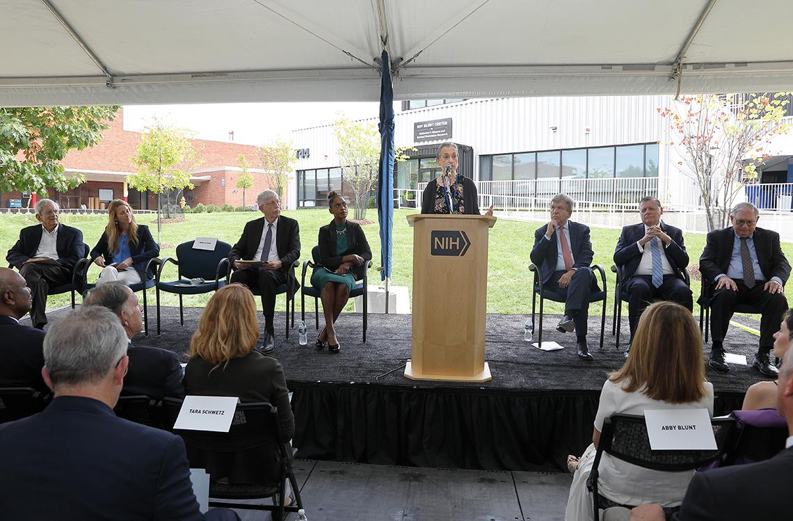 Several speakers sit on stage watching Schor speak from a podium