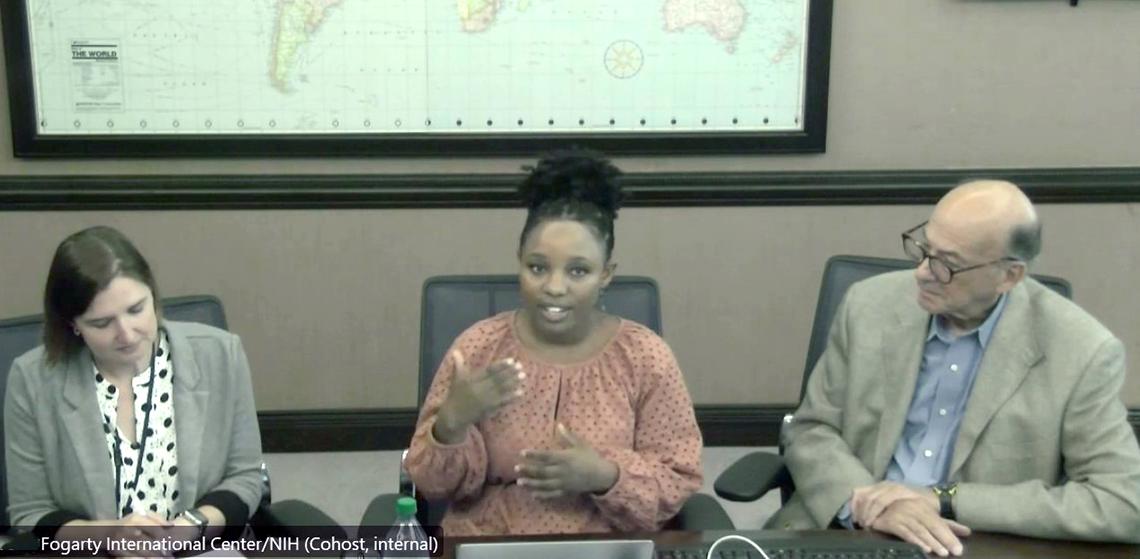 Humure, Coan-Stevens and Glass sit at conference room table, world map behind them