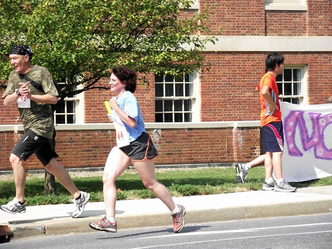 Iskhakov, on the sidewalk, runs alongside Derbyshire, on the racecourse.