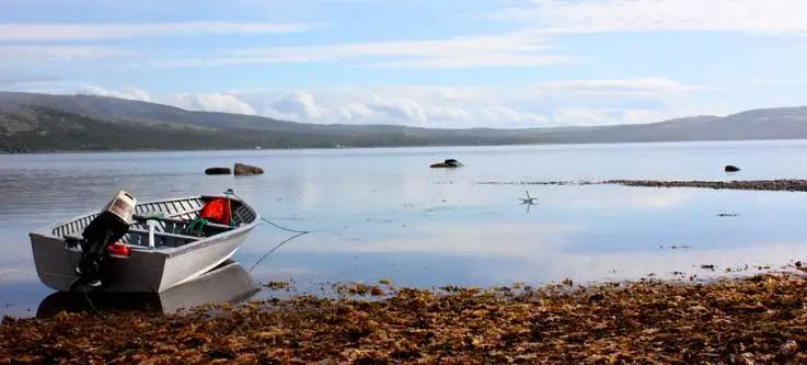 Boat at shoreline with water and mountains and stretched on the horizon
