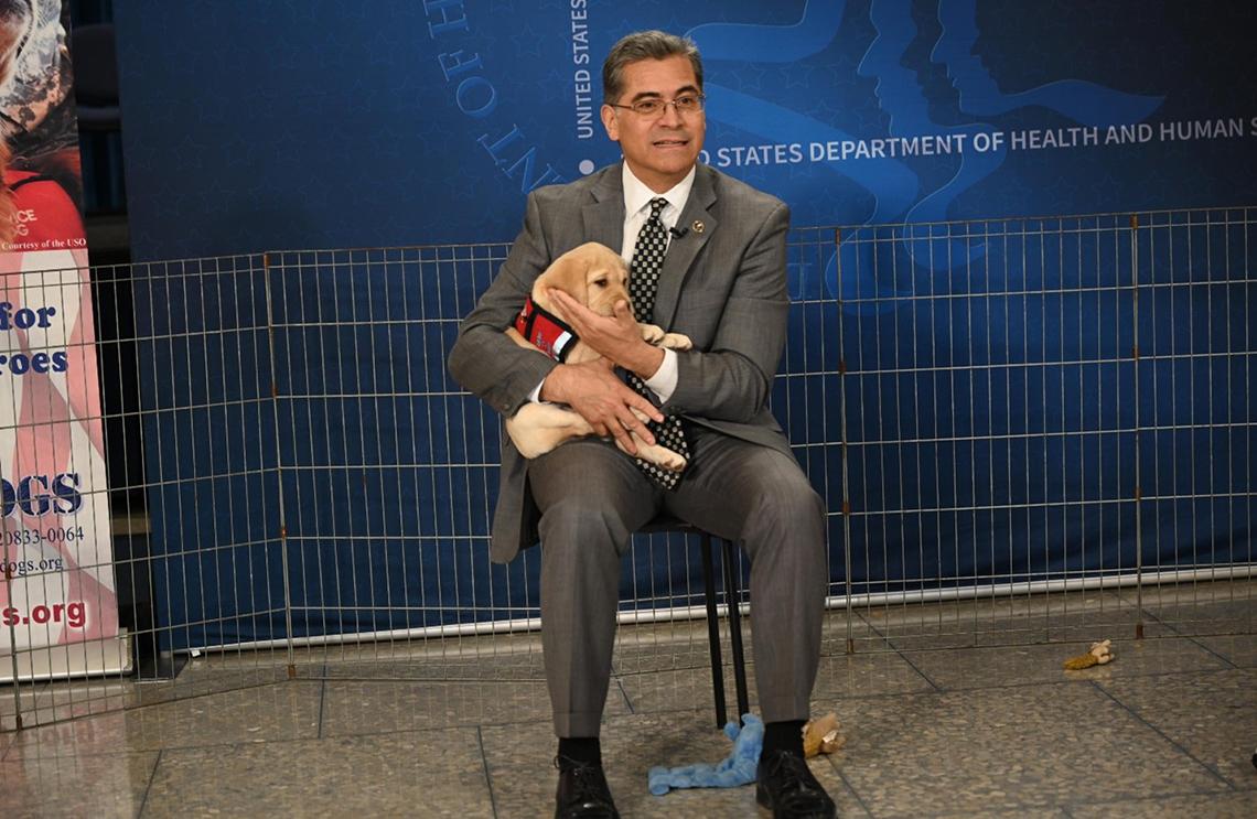 Becerra sits on chair, cradling puppy in his arms.