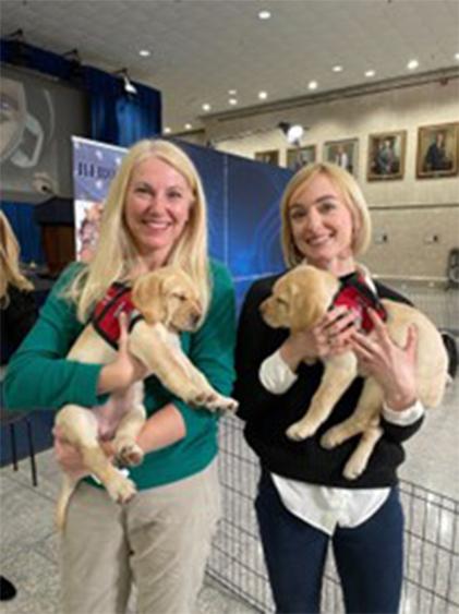 Weber and Quinlan stand smiling each holding sleepy puppies.