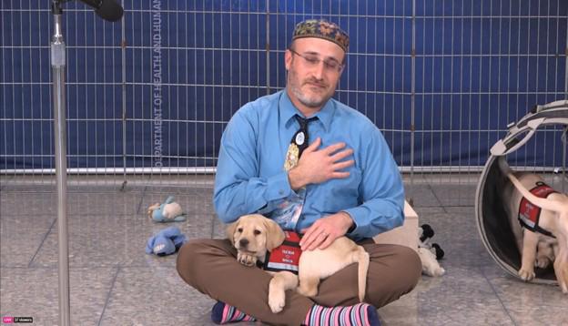 Zoosman, with hand over his heart and eyes closed, meditates with puppy sprawled out on his lap.