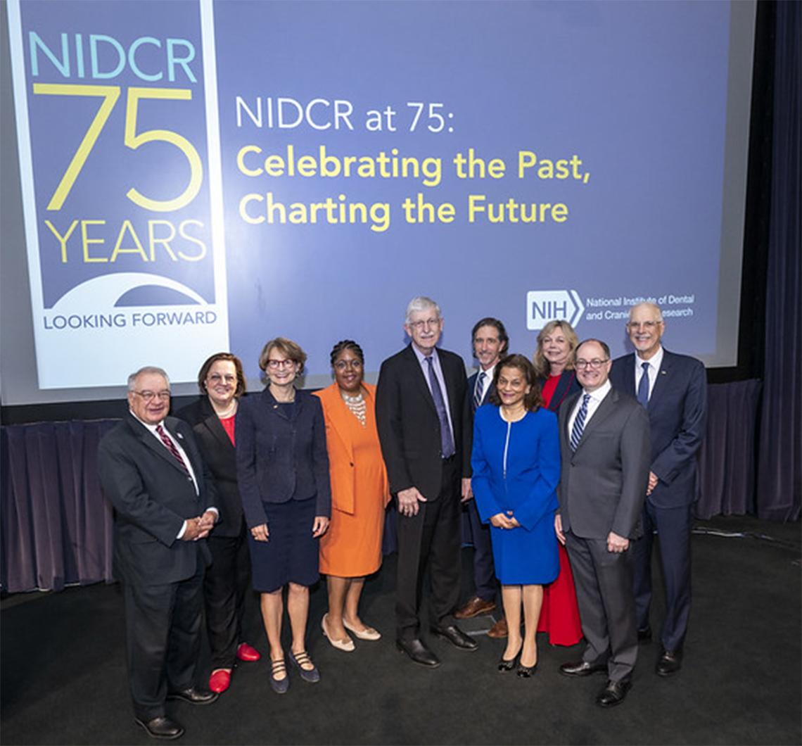Group shot of meeting participants in front of NIDCR 75 Years slide in Lipsett Amphitheater