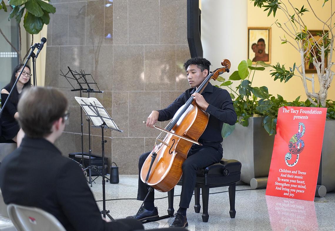 Man holds bow to cello while looking at sheet music on music stand.