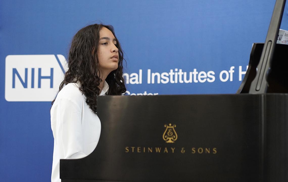 A woman looks out at audience while playing piano.