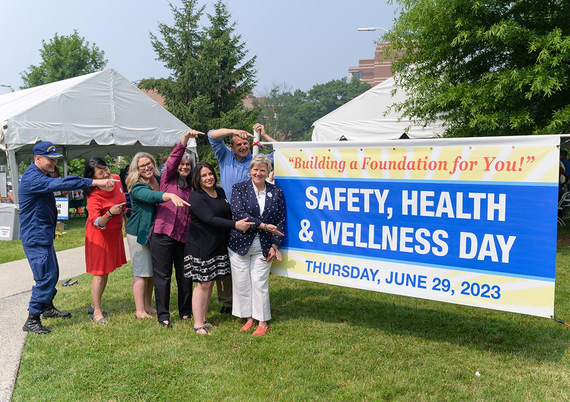 NIH leaders hold up Safety, Health &amp; Wellness Day 2023 poster outside on the lawn