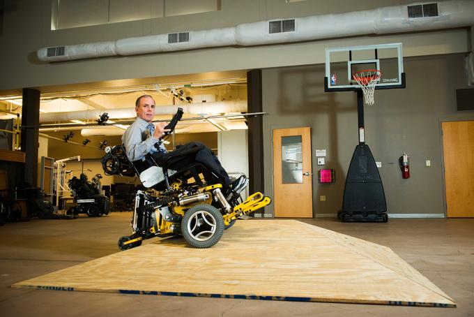 Cooper in MEBot power wheelchair, in gymnasium with basketball hoop