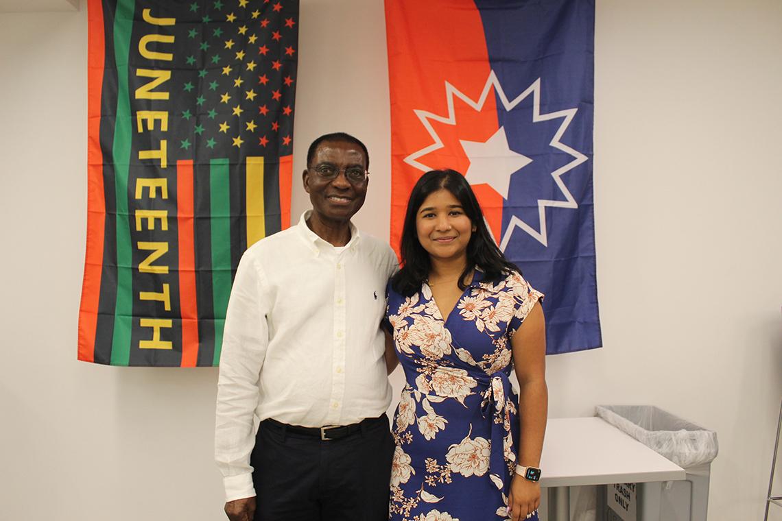 Two people stand in front of the Juneteenth flag