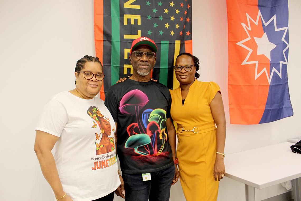 3 Attendees stand in front of a Juneteenth flag 