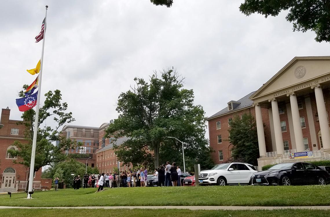 A crowd gathers around the Bldg. 1 flag pole