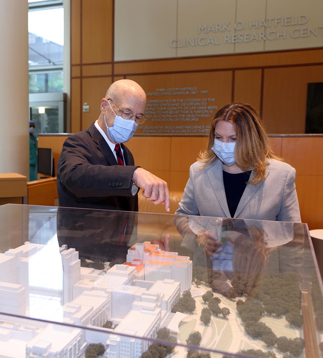 Gilman points to where the new wing will be on the model as Palm looks on