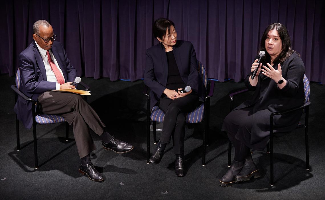 Dr. Wojcik talks into the microphone, palm open, as two panelists listen.