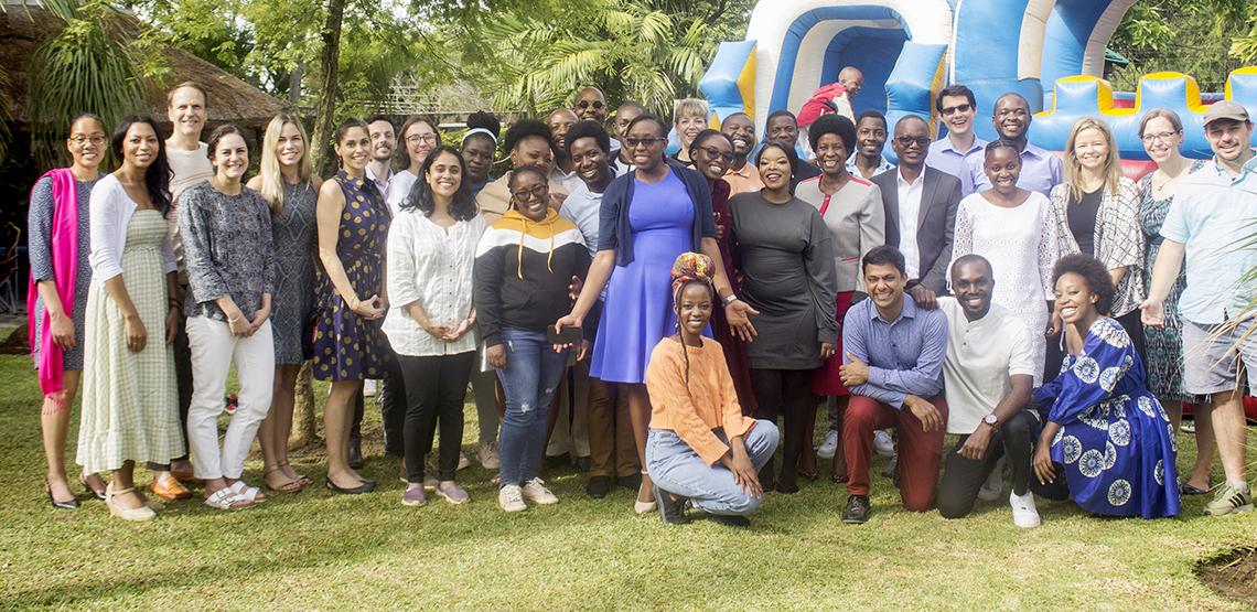 Large group of people stand outdoors in front of moon bounce as kids play in background