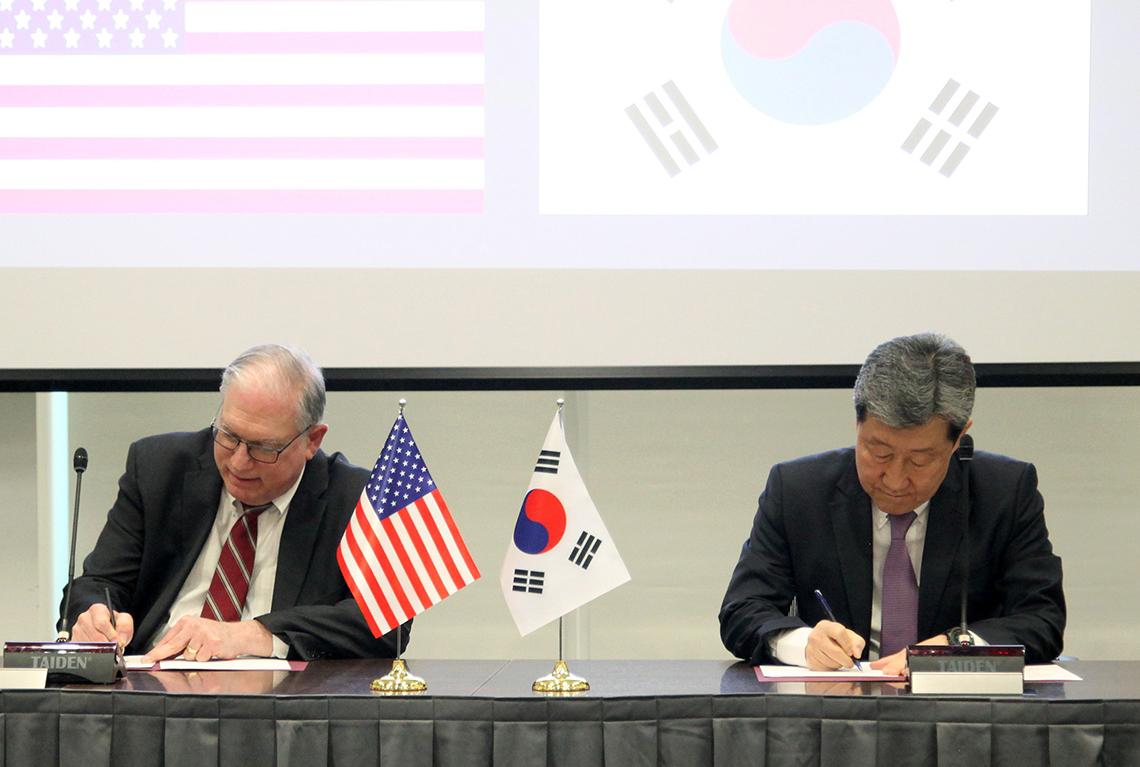 Tabak seated beside Dr. Cha Soon Do, both signing papers