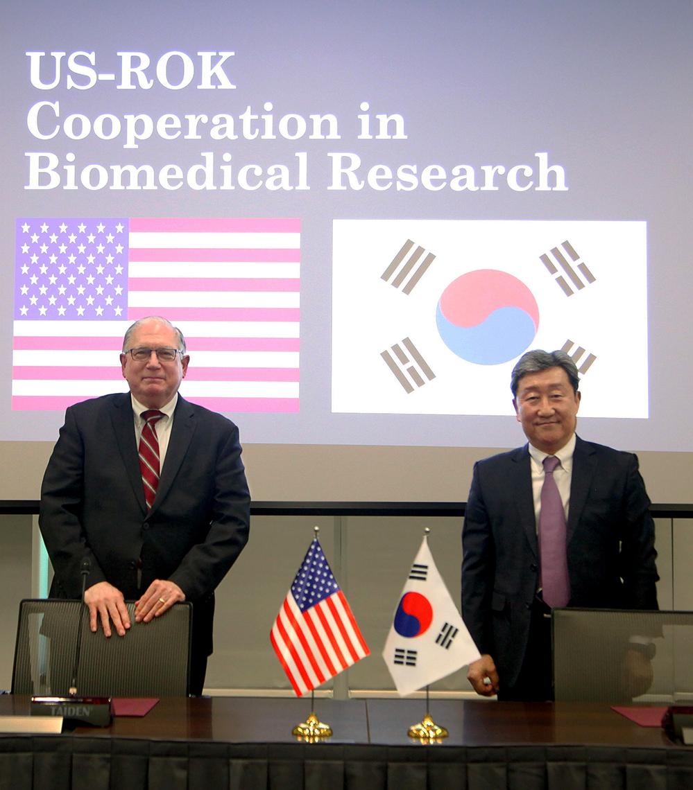 Tabak beside Dr. Cha Soon Do, with country flags and agreement title slide projected on screen behind them